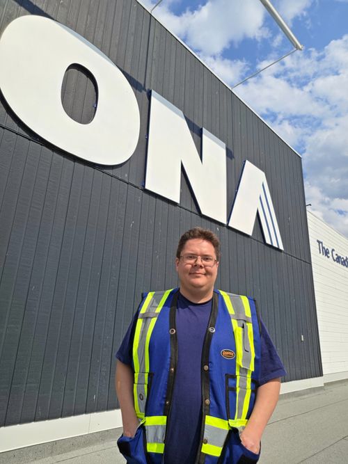 Man in blue and yellow safety vest standing in front of RONA building