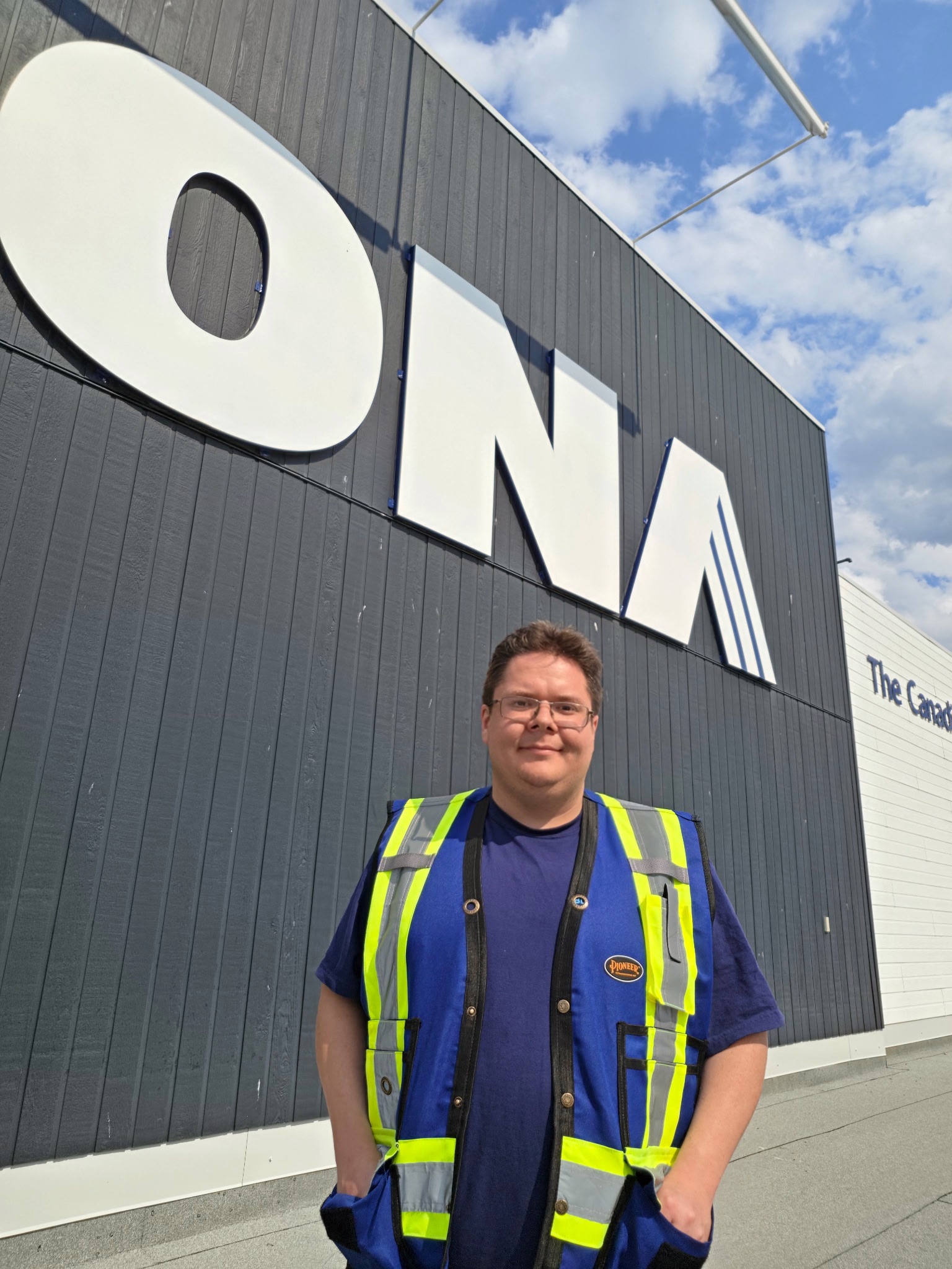 Man in blue and yellow safety vest standing in front of RONA building