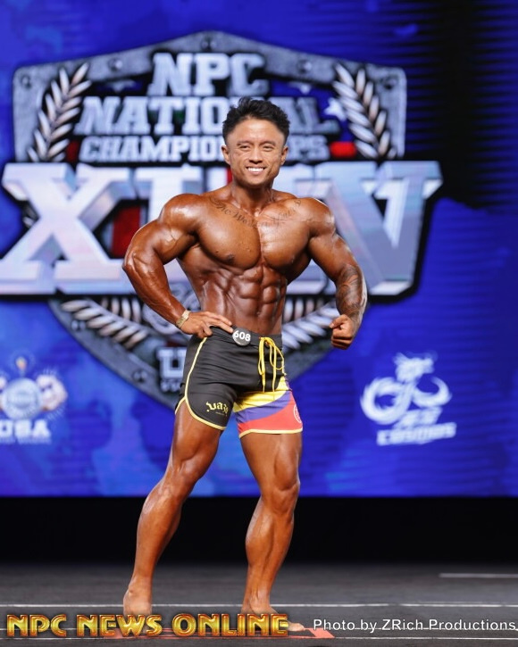 Bodybuilder posing on stage presenting muscular physique under bright lights at NPC National Championships.