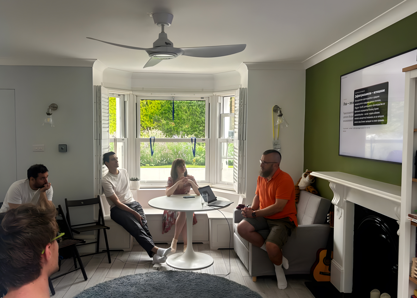 A group of people sitting in a room, talking and looking at the screen with a presentation on it 