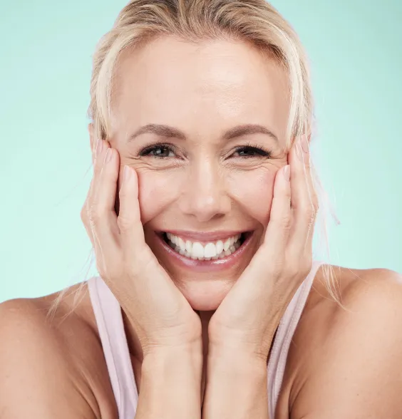 A woman smiles brightly, her hands gently cupping her face, showcasing her healthy teeth and joyful expression