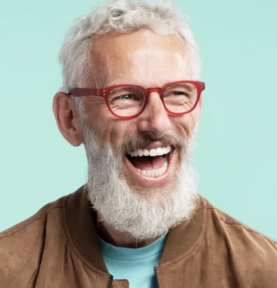 A man with glasses and a beard joyfully laughing, showcasing a bright smile and healthy teeth