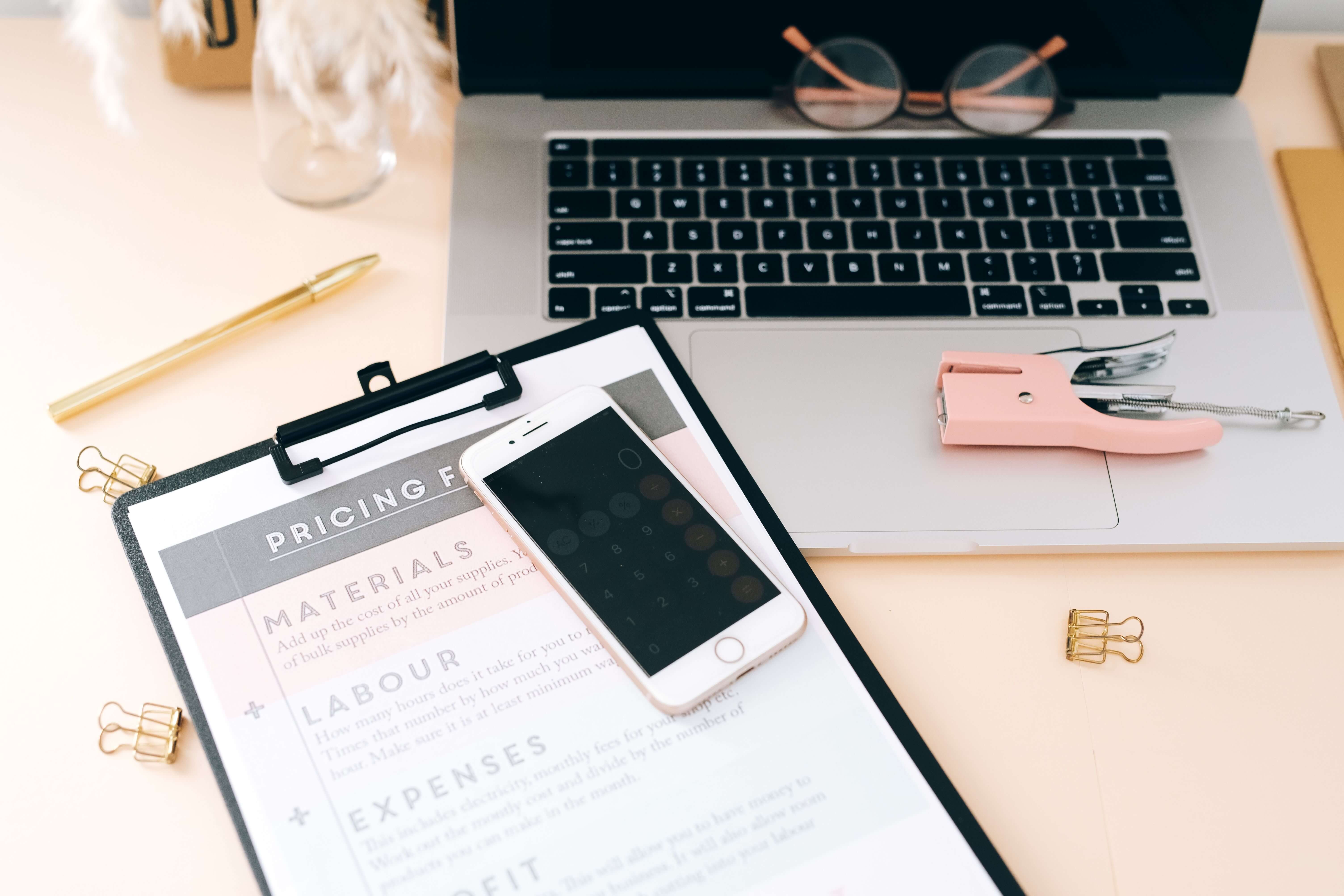 Calculations and pricing worksheet next to a laptop for small business expense and payroll planning.