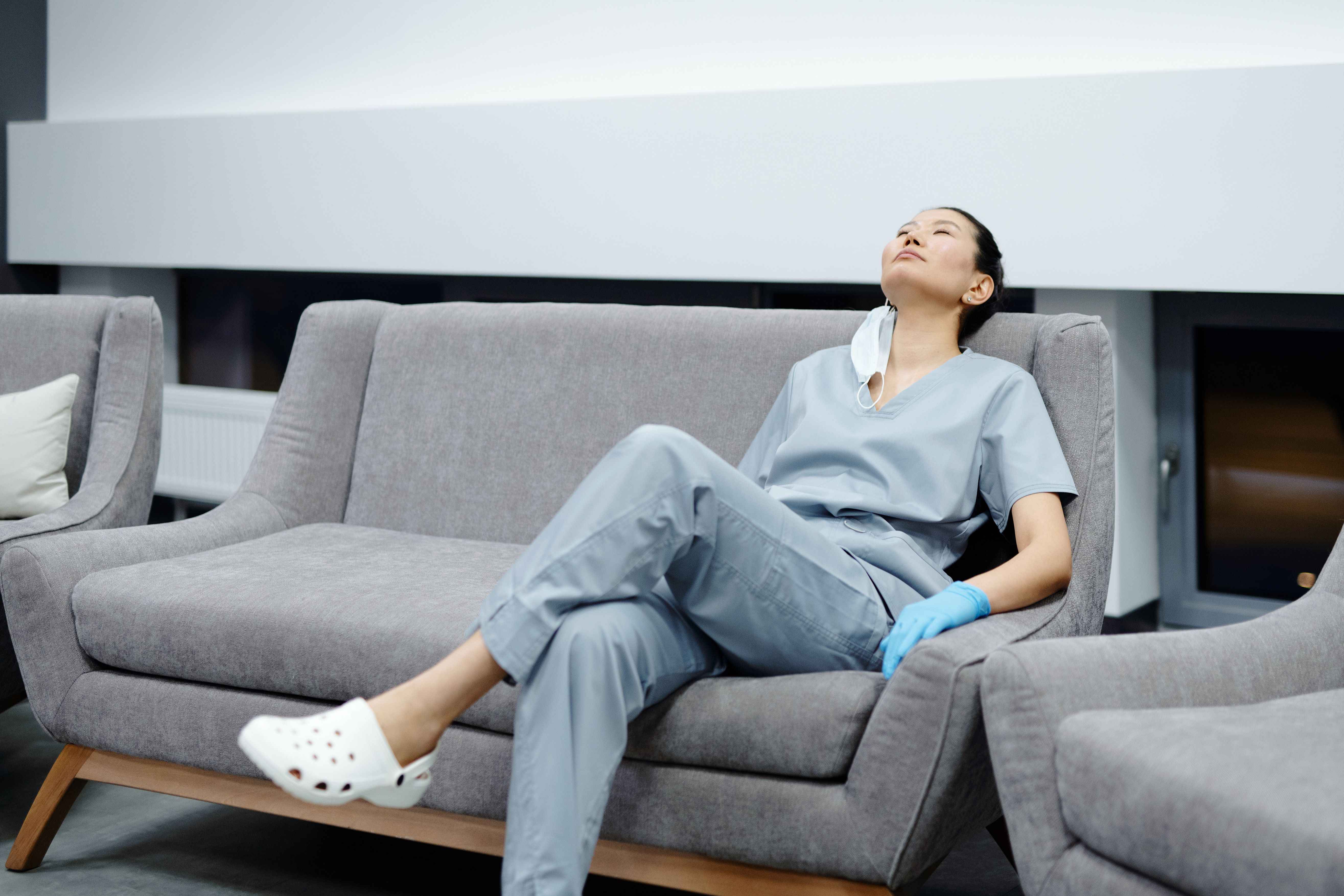 Nurse in light blue scrubs resting in a hospital waiting area, holding a blue medical glove after a shift.