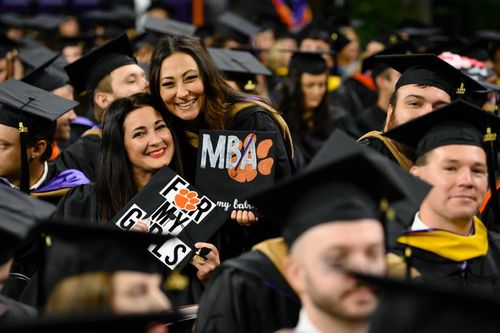 Clemson MBA Students Smiling at Graduation. Two women holding small signs that includes "for my girls" and "MBA".