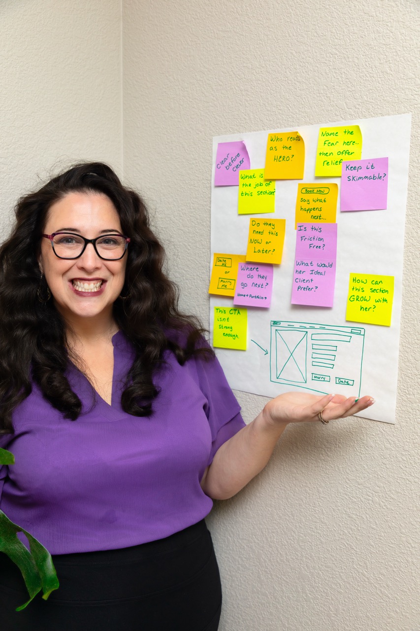 Lizzy Moffett smiling next to whiteboard with colorful sticky notes and website wireframe