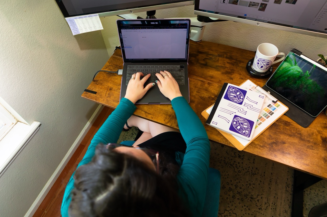 Lizzy Moffett working at desk with laptop, tablet, and design sketches for a 2-day Website