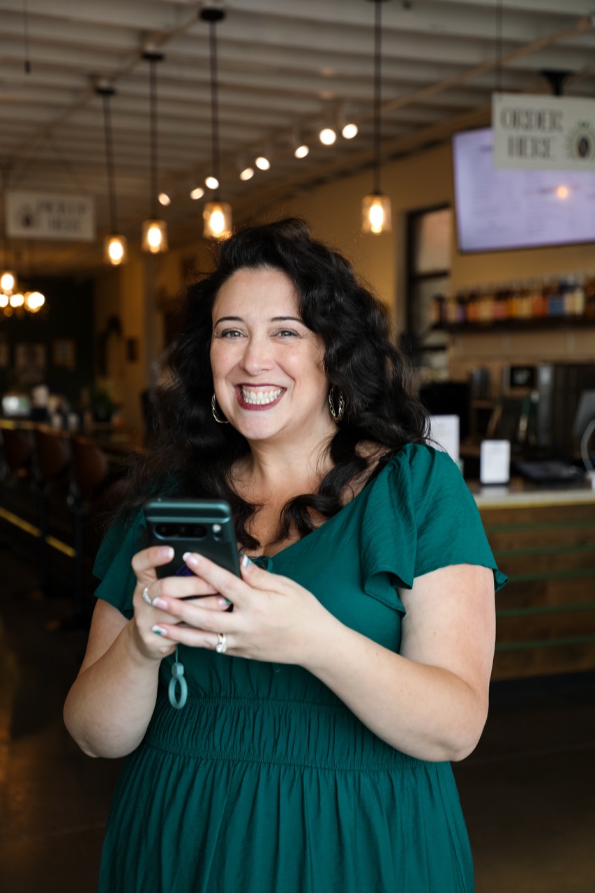 Lizzy Moffett in green dress using smartphone in cozy cafe