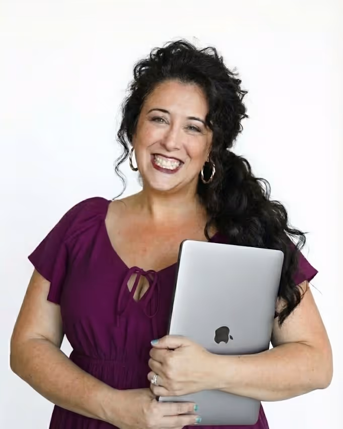 Lizzy Moffett smiling and holding a laptop, wearing a purple top