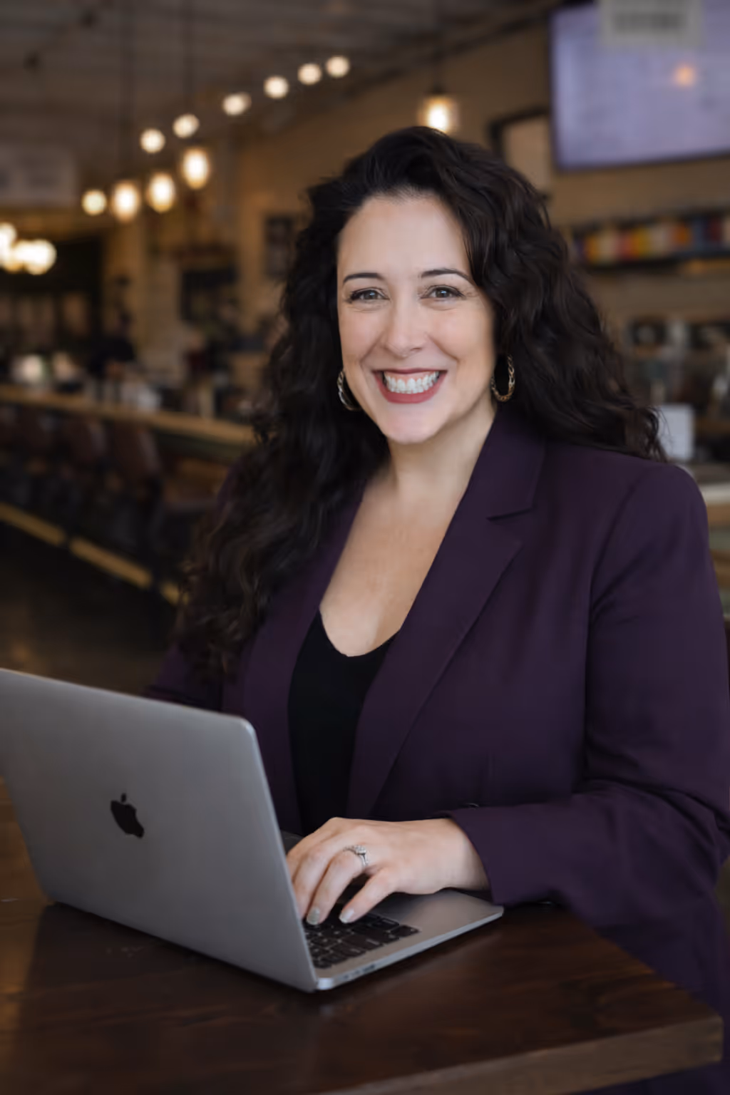 Lizzy Moffett smiling while working on laptop in coffee shop