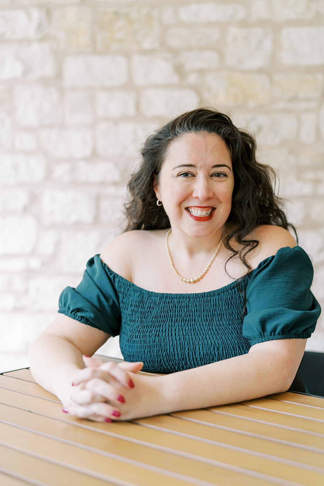 Lizzy Moffett smiling portrait wearing teal off-shoulder top at table
