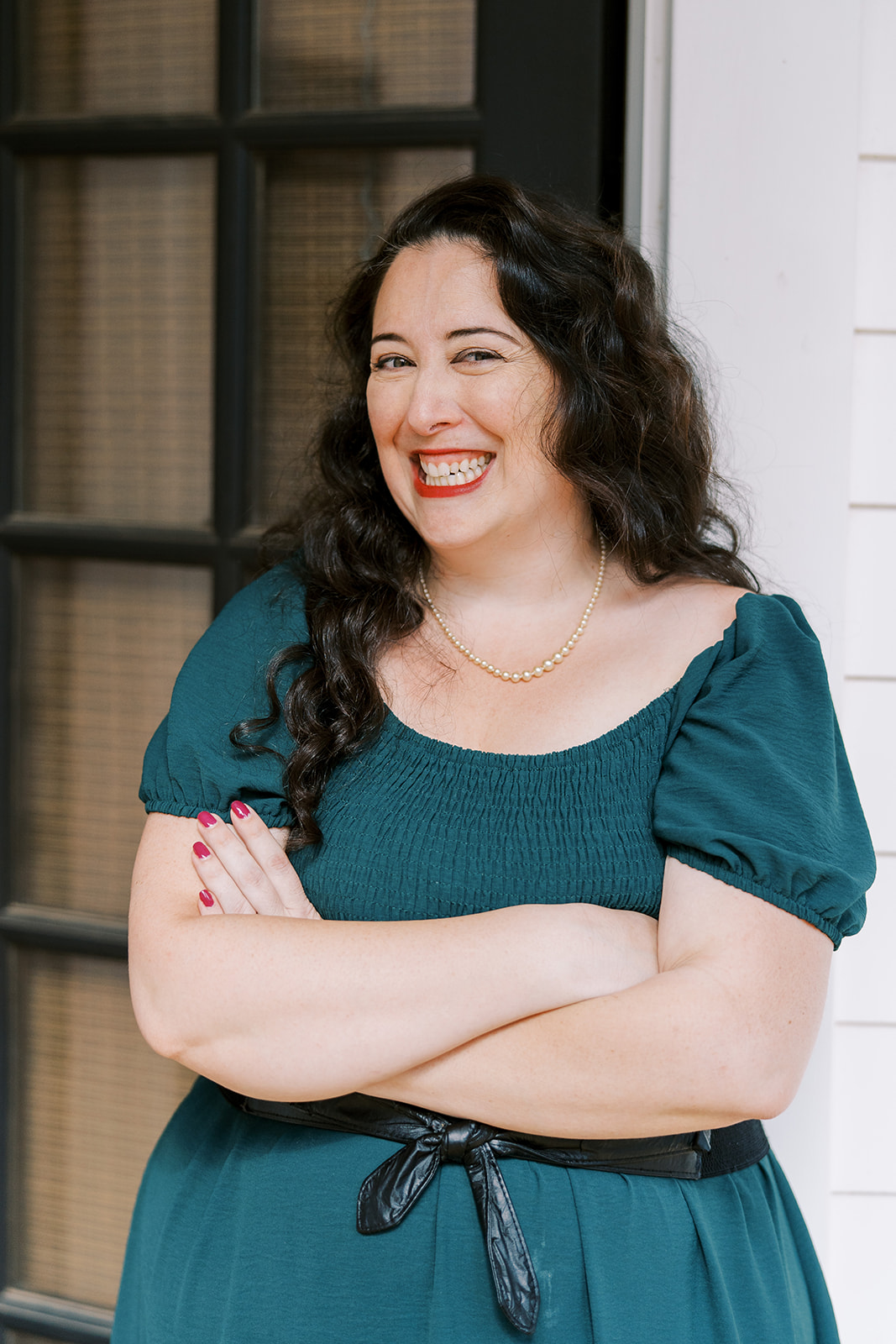 Lizzy Moffett smiling, wearing teal dress with pearl necklace and red nail polish