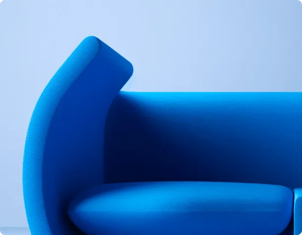 Close-up of a modern blue upholstered sofa with curved armrest against a light blue background.