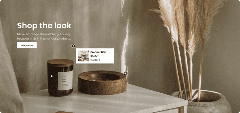 A modern white table holding a dark candle jar and a wooden bowl with pampas grass in a large pot beside it, featuring interactive product hotspots.