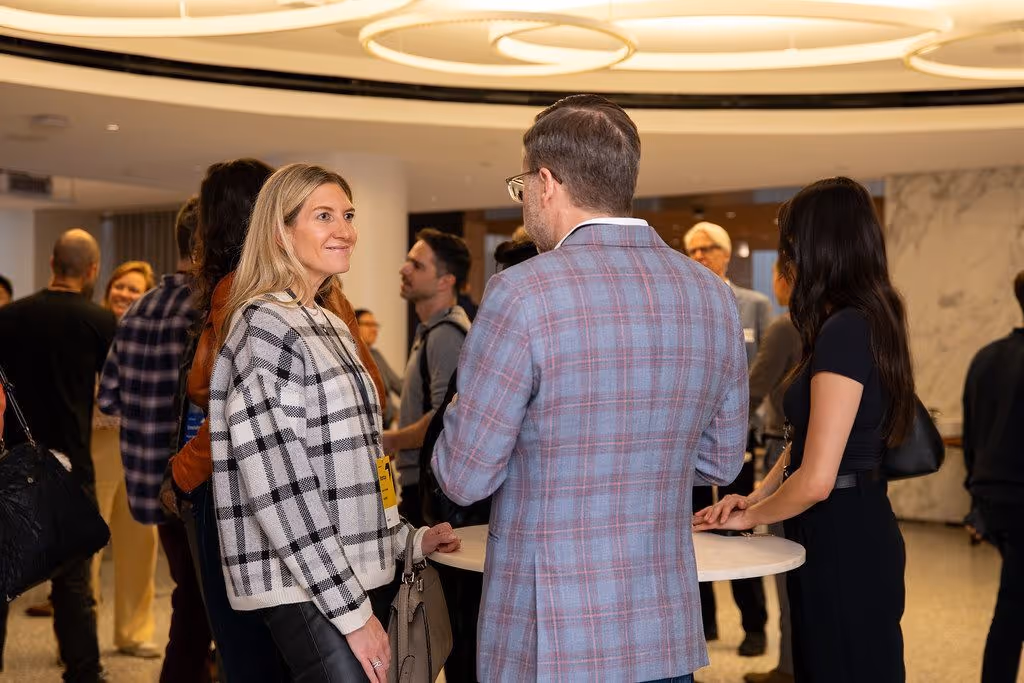 Professionals networking at a venture capital event, engaging in conversations around a cocktail table in a modern office setting.