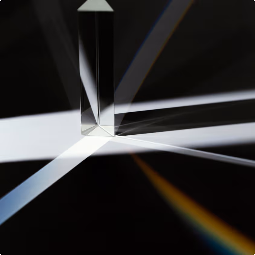 Glass prism refracting and dispersing light into multiple beams and subtle rainbow colors on a black background.