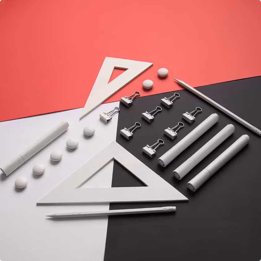 White stationery items including rulers, pens, binder clips, erasers, and pencils arranged on a red, black, and white geometric background.