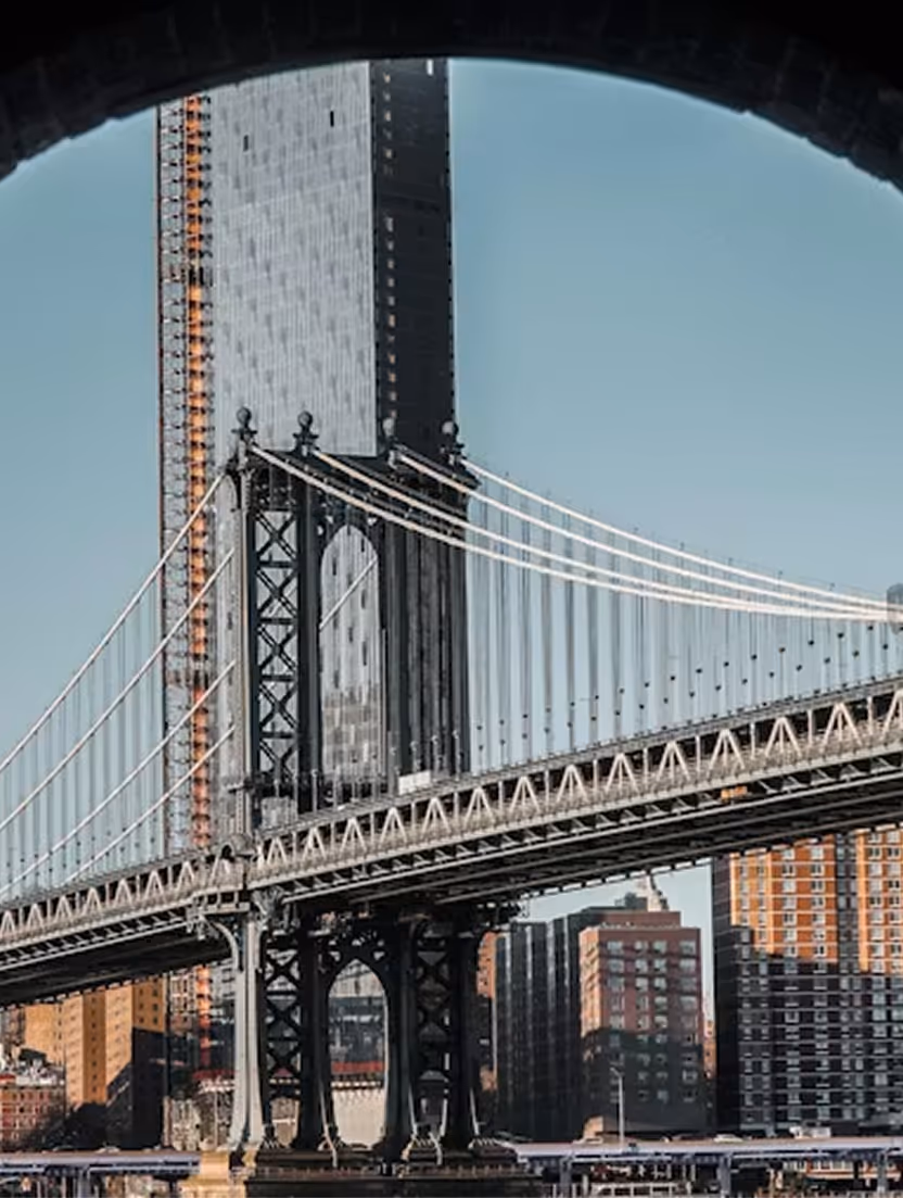 View of a suspension bridge and city skyscrapers framed by a dark archway.