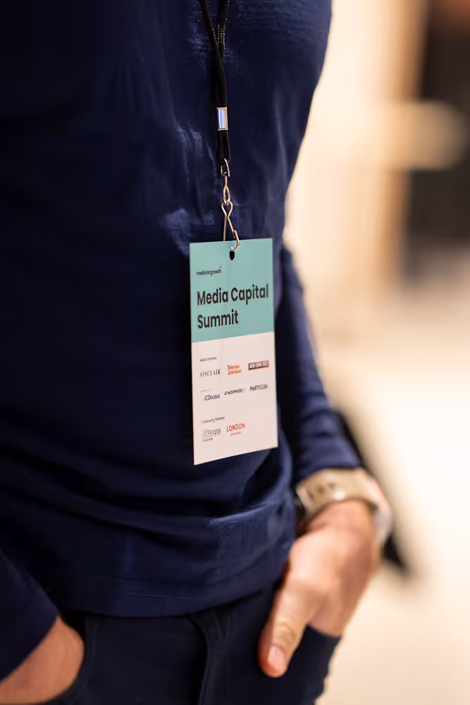 Person wearing a navy shirt with a Media Capital Summit badge hanging from a black lanyard.