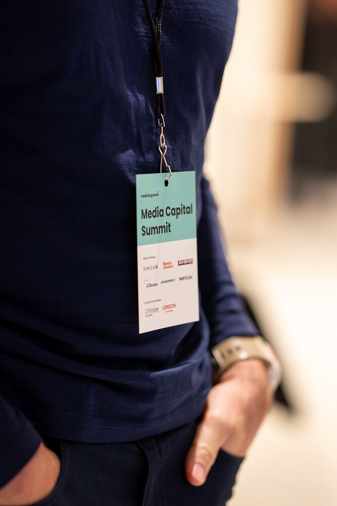 Person wearing a navy shirt with a Media Capital Summit badge hanging from a black lanyard.