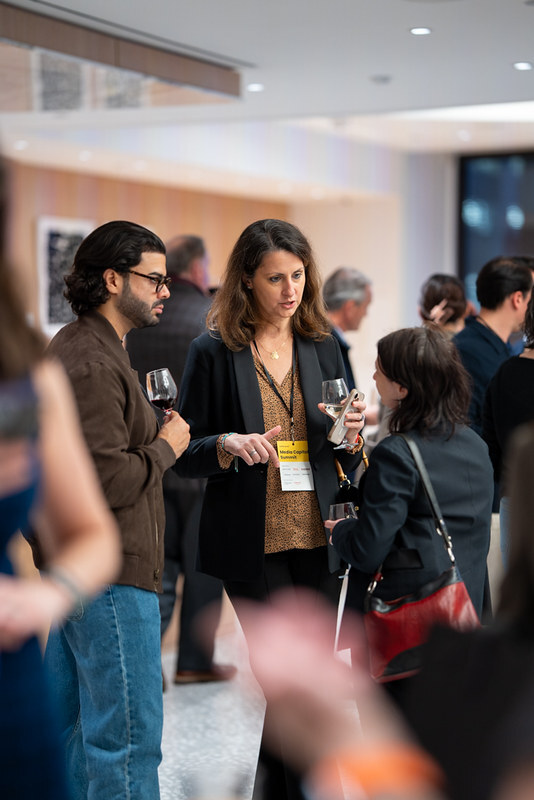 Three adults engaged in conversation at a social or networking event, holding drinks indoors.