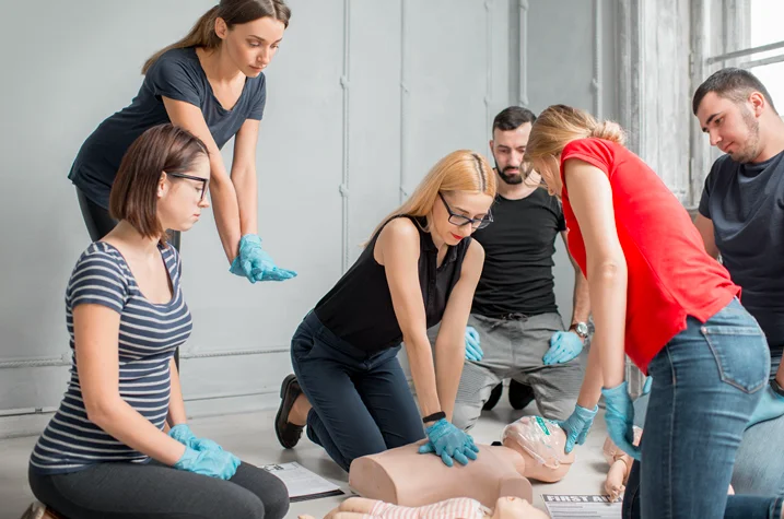 Group practicing CPR on training dummy with instructor guidance during first aid training session in classroom setting