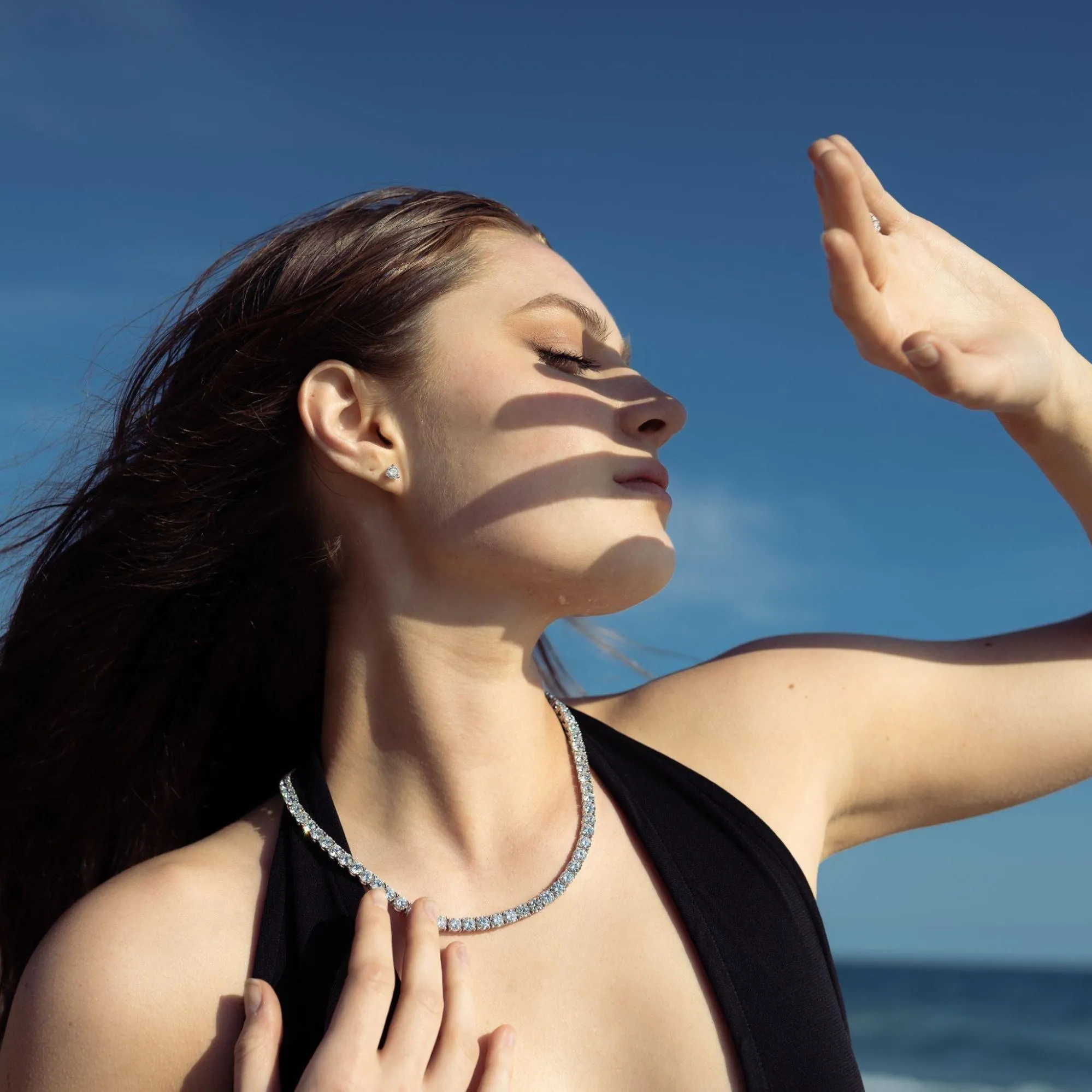  Lab grown diamond  tennis necklace and stud earrings worn by a woman in sunlight near the ocean