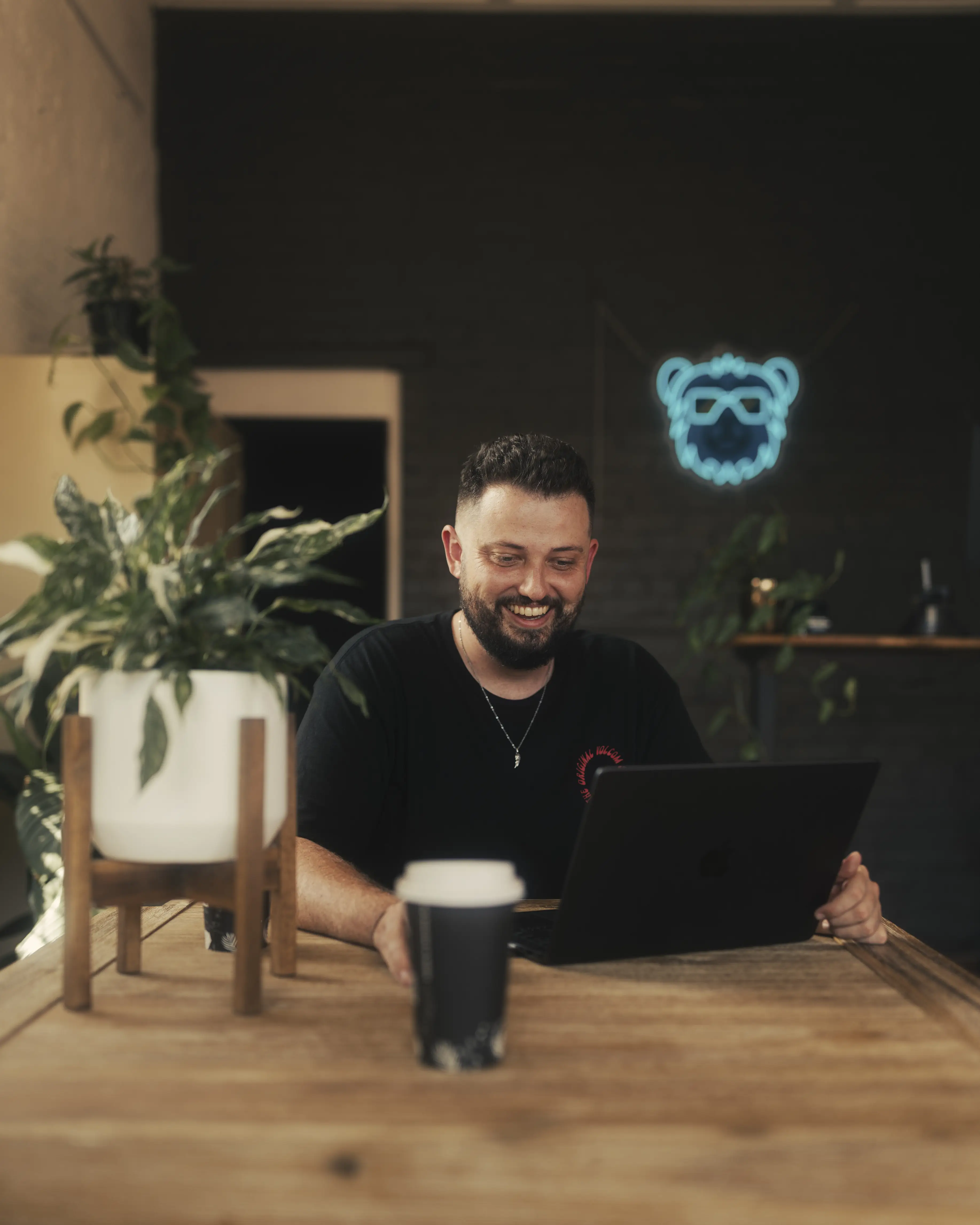 Robbie, Founder of Tudgee, smiling at laptop talking to a client on a video call with a coffee on the table