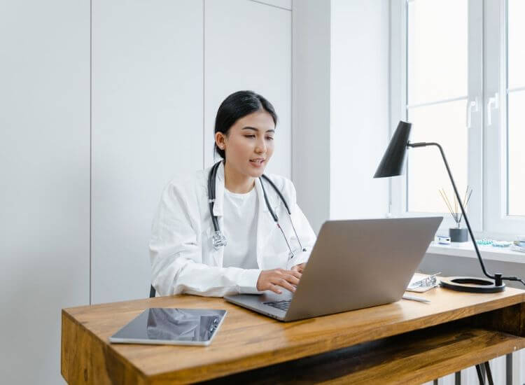 A doctor speaking with a patient through a video meeting on a laptop in a medical office