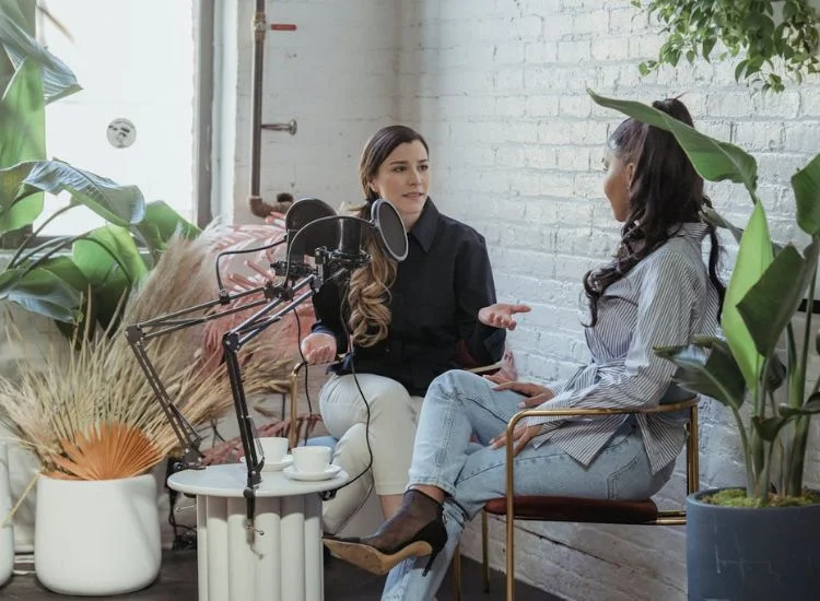 A host interviewing a guest for a podcast with two microphones set up on a table
