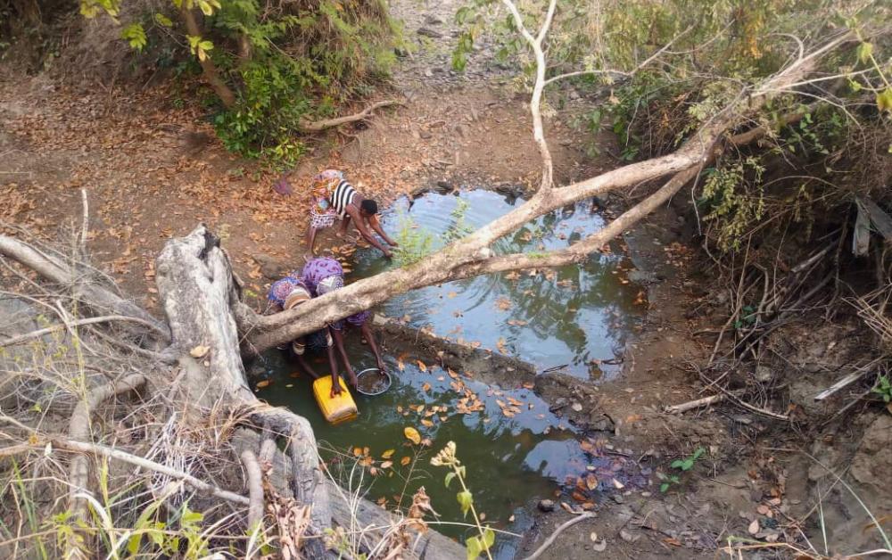 Eine unhygienische Wasserstelle in Benin, aus der 3 Frauen Wasser schöpfen
