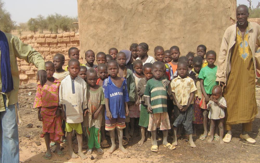 Gruppe burkinischer Kinder vor einer Lehmmauer – ländliche Armut und fehlender Zugang zu Bildung.