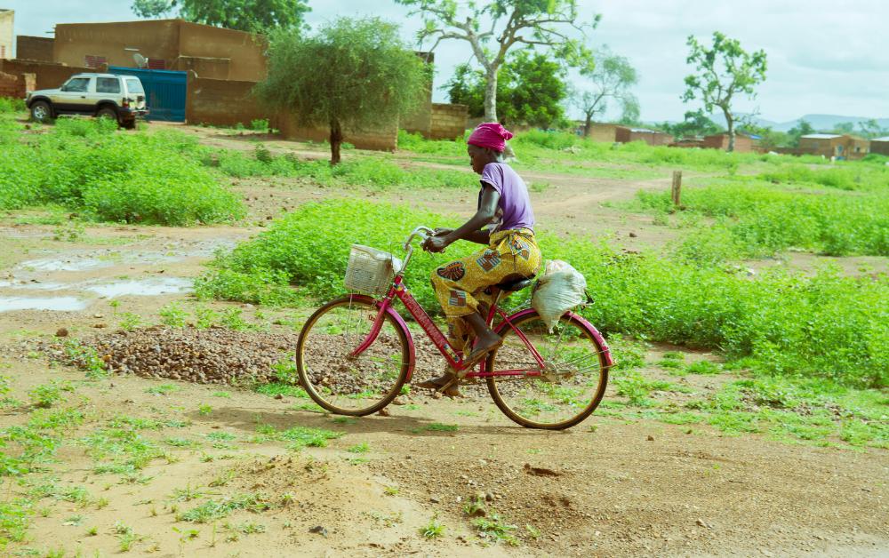 Burkinische Frau auf dem Fahrrad in ländlicher Umgebung – Alltag und Mobilität in Westafrika.