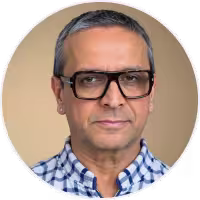 Portrait of a middle-aged man with short gray hair wearing large black glasses and a blue checkered shirt.