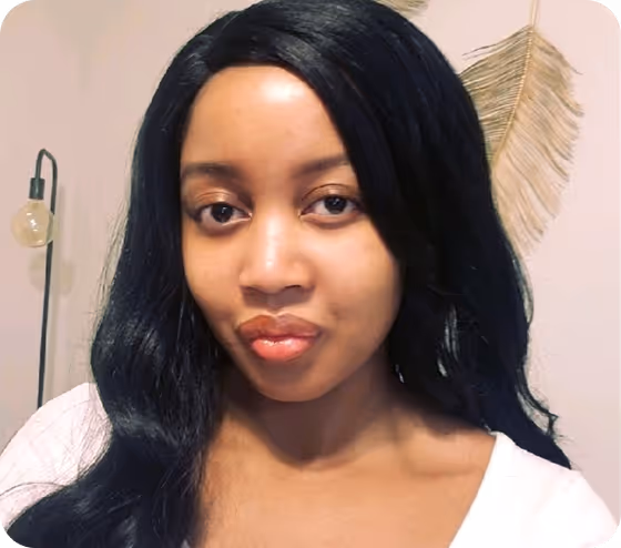 Woman with long black hair wearing a white top, sitting indoors with a decorative leaf and lamp in the background.