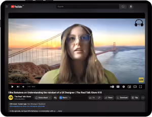 YouTube video on a tablet screen showing a woman with glasses and headphones speaking, with the Golden Gate Bridge at sunset as her virtual background.