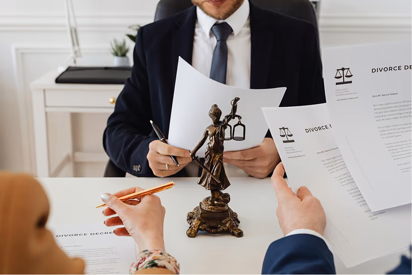 Two people reviewing divorce decree papers across a desk with a Lady Justice statue between them.