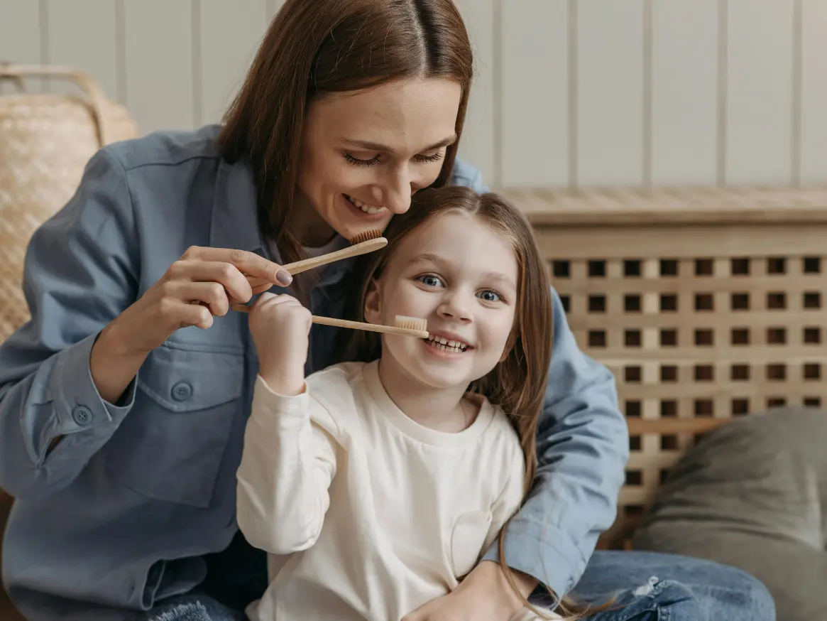 Mum and young daughter brush their teeth together as the mother supervises.