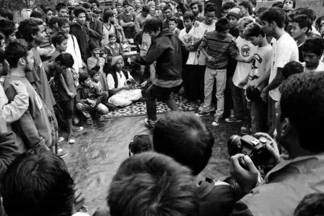 Une foule regarde une personne danser au centre d'un cercle animé lors d'un événement en plein air.