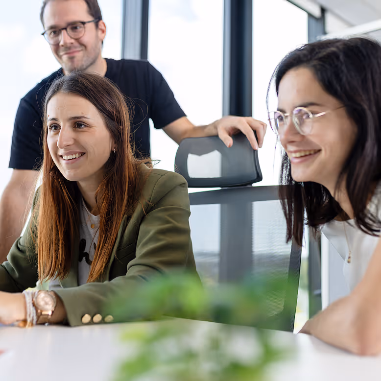 Trois jeunes professionnels souriants réunis en réunion dans un bureau lumineux.