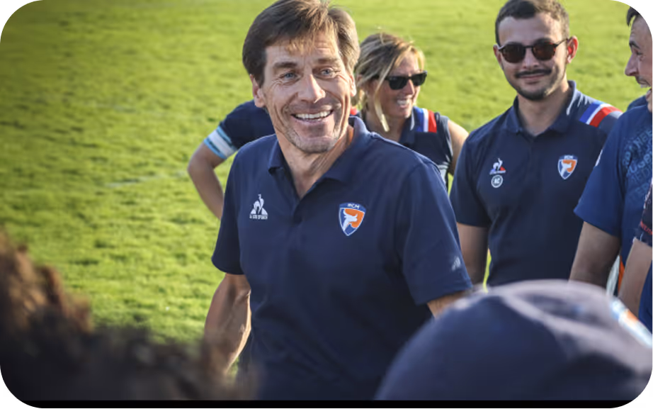 Des membres d'une équipe de rugby souriants en polo bleu sur un terrain herbeux au soleil.