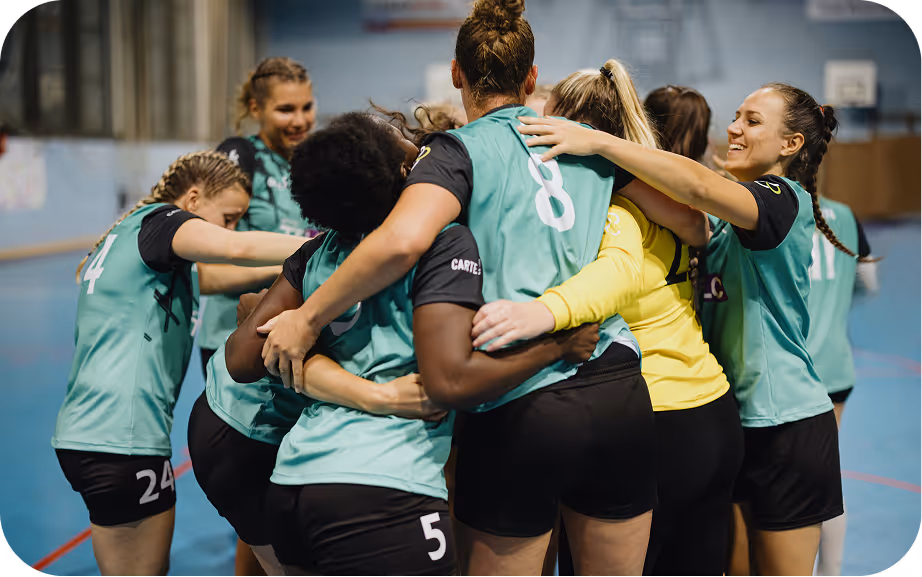 Une équipe de sport féminine portant des maillots verts s'enlace et célèbre ensemble dans un gymnase.
