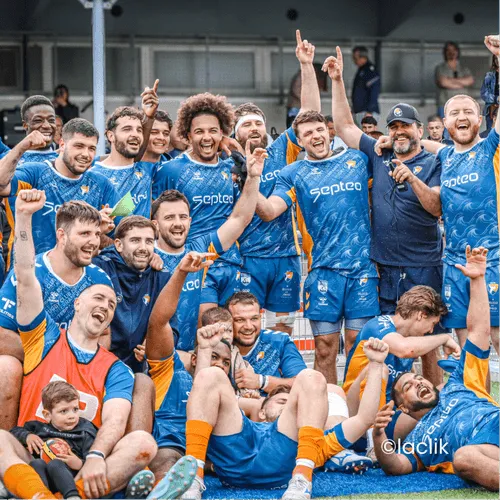 Joueurs de rugby courant sur le terrain devant des pom-pom girls et une foule enthousiaste dans les gradins.
