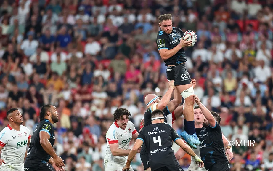 Joueur de rugby en maillot bleu foncé tenant un ballon ovale lors d'un match sur le terrain.