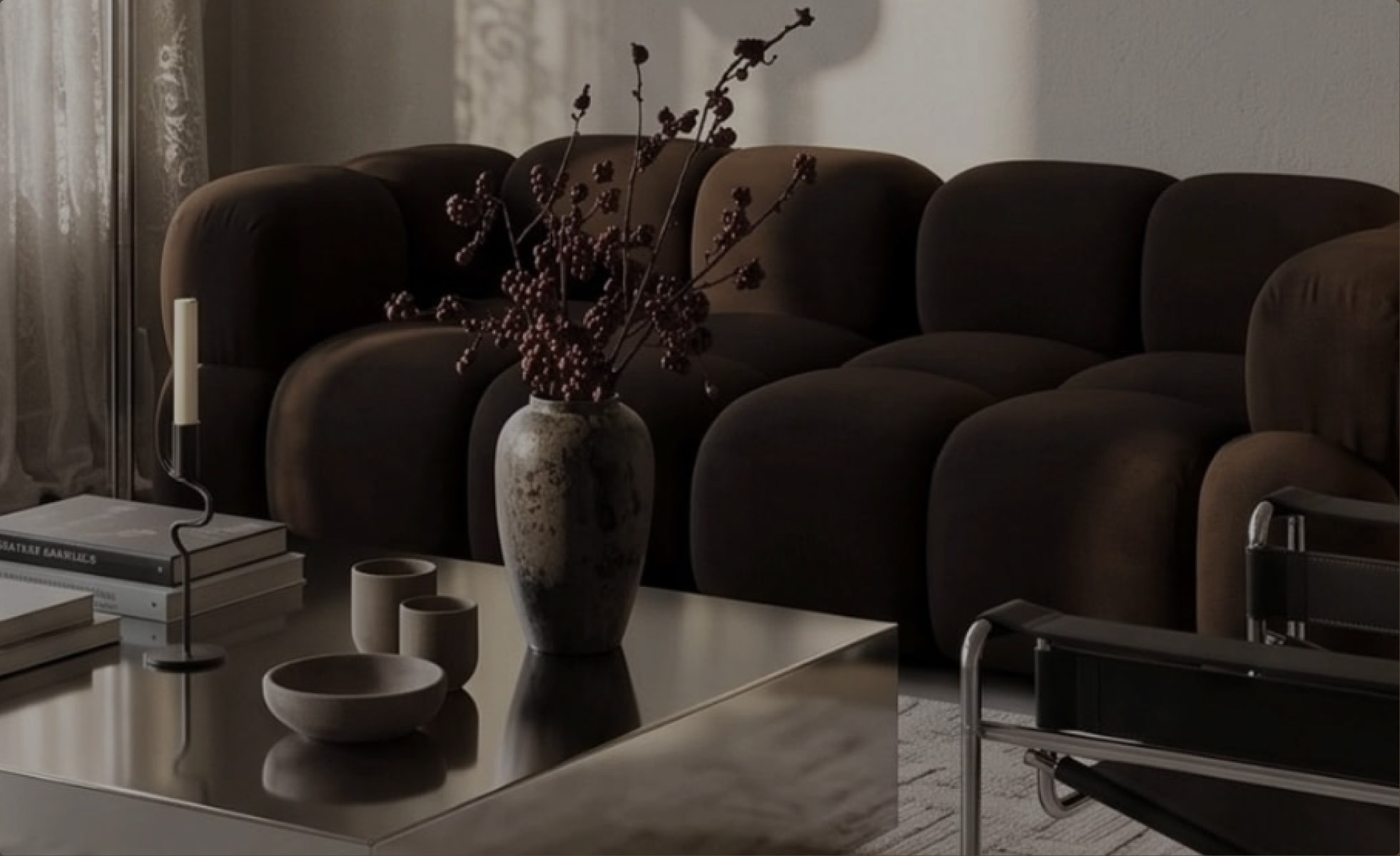 A dark, warm living room with a brown modular sofa, a stone vase of berry branches and a glass coffee table