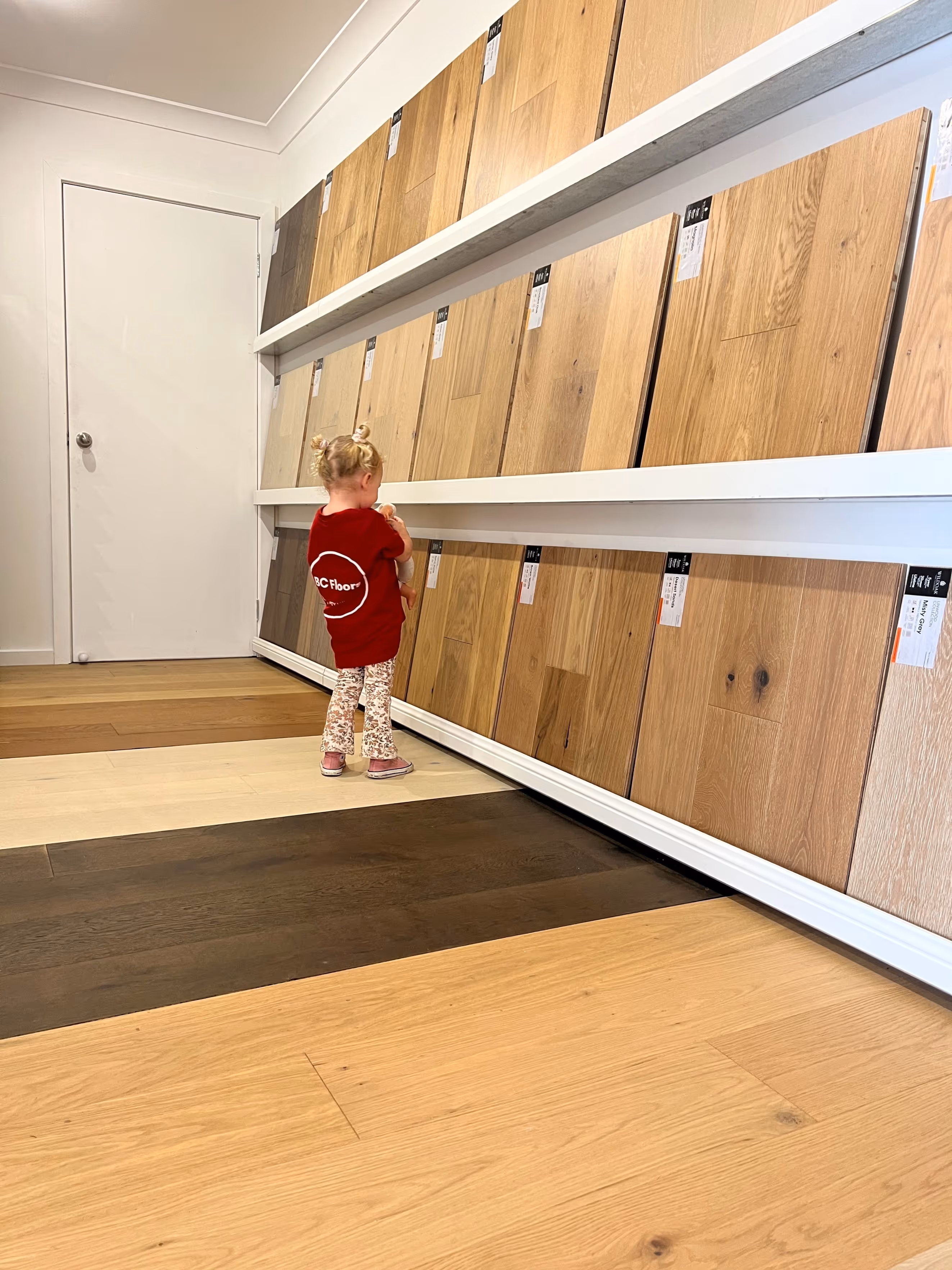 Child looking down at a display of laminate flooring samples in a showroom. The various wood tones and finishes showcase different style options.