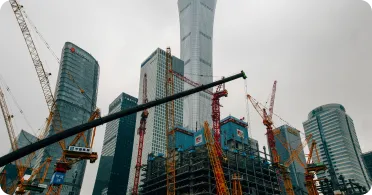 Construction site with multiple cranes and skyscrapers under an overcast sky.