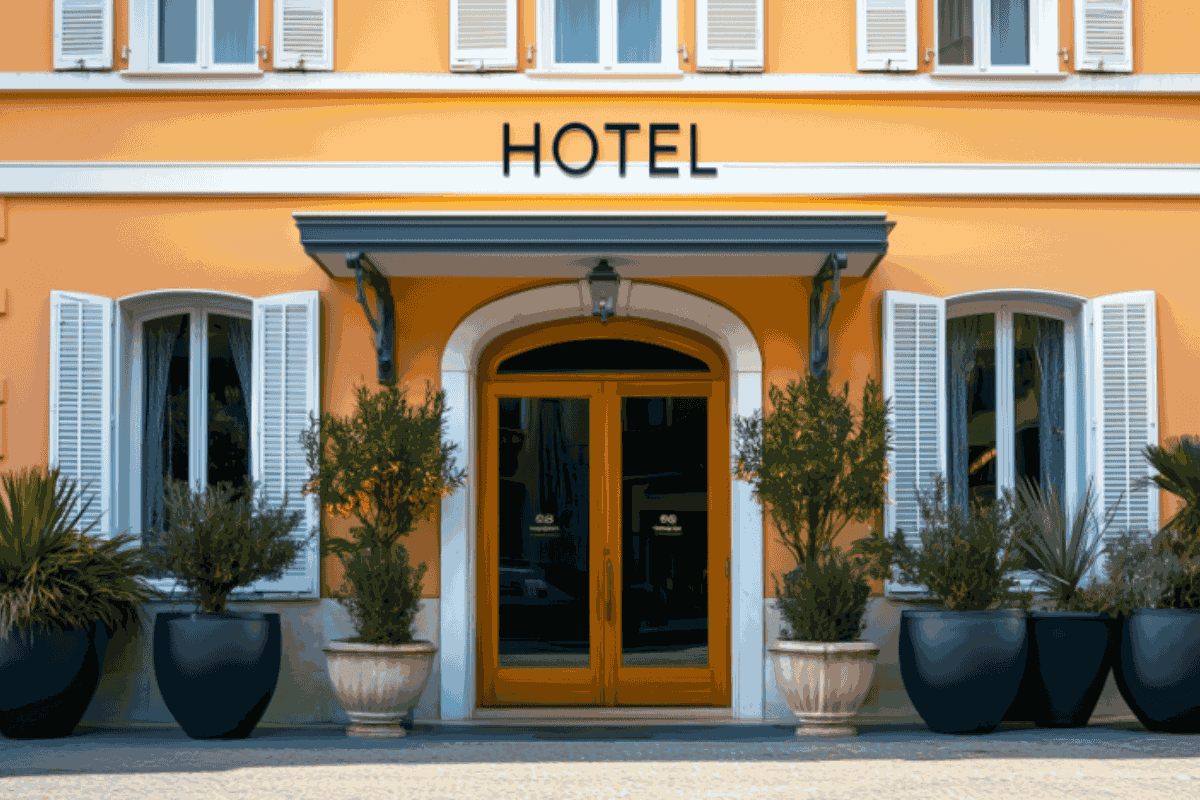 Entrée d’un hôtel avec porte en bois, volets blancs et plantes décoratives, représentant l’environnement des hôteliers adoptant des solutions d’IA sécurisées et souveraines.