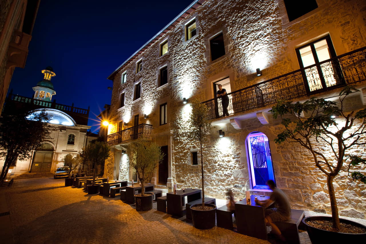 Façade d’hôtel en pierre éclairée de nuit avec terrasse extérieure et ambiance chaleureuse.