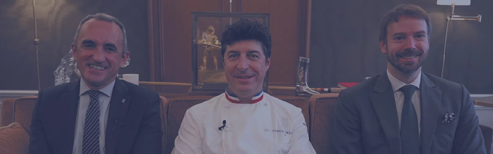 Trois professionnels de la restauration en tenue formelle et veste de chef, assis côte à côte.